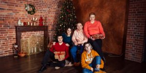 A family posing with Christmas gifts by a decorated tree indoors, exuding holiday warmth.